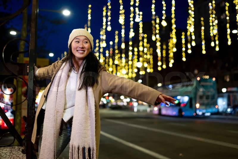 Happy young girl enjoying christmas lights in the street. Beautiful woman having fun at night in the city during winter.