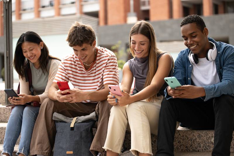 Multiracial young people sitting in stairs while texting.Cheerful group of friends using their phones in the street.