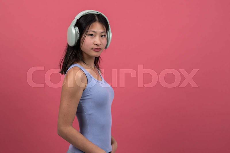 Confident woman with headphones looking to the camera. Proud young female listening to music isolated on a red background.