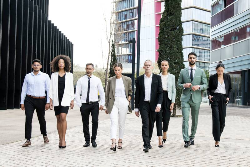 Group of confident business people walking the street together looking at camera. Diverse team of successful businesswoman and businessman walking outside.