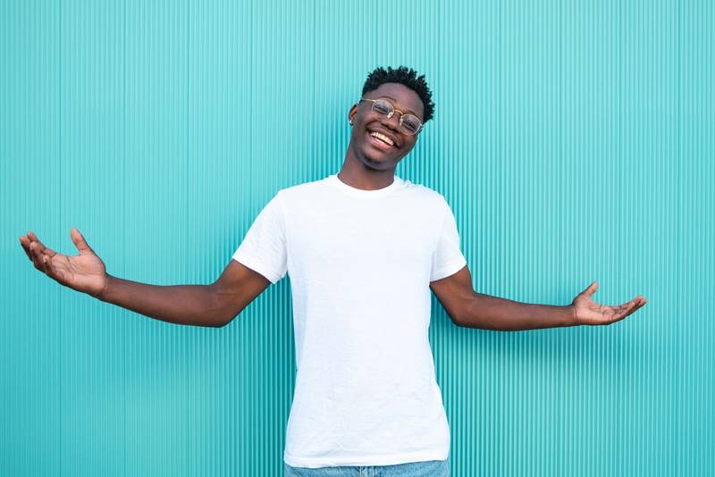 Portrait of a happy african american guy smiling with his arms wide open on turquoise background and white t-shirt.