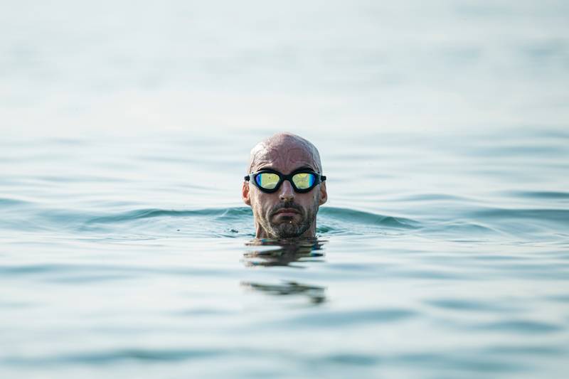 Confident man swimming in the ocean wearing glasses looking at camera. Swimmer pulling his head out of the water focused.