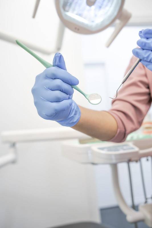 dentist wearing surgical gloves, holding professional instruments