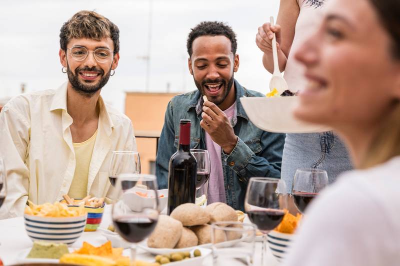 Happy group of friends eating and drinking in a terrace table. Young relaxed people having rooftop dinner party.