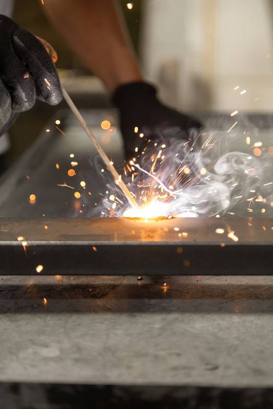 hands of a person wearing black protective gloves while using a metal welding tool