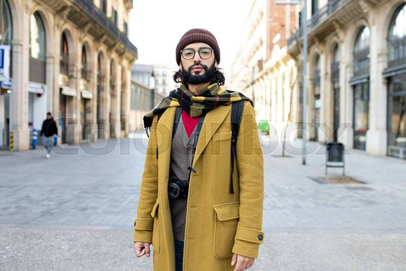 Young tourist with beard standing at the city looking at camera. Front view of a hipster male in Barcelona. Travel concept. 