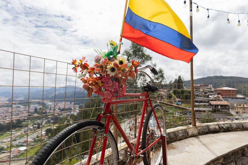 vintage-style bicycle stands adorned with bright flowers beside a proudly waving flag