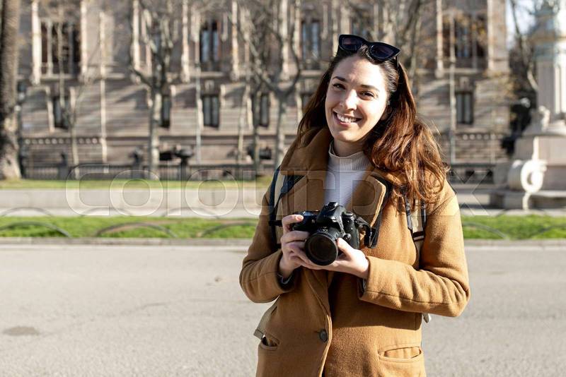 smiling woman traveler holding a camera at the city in holidays - relaxation, tourism concept