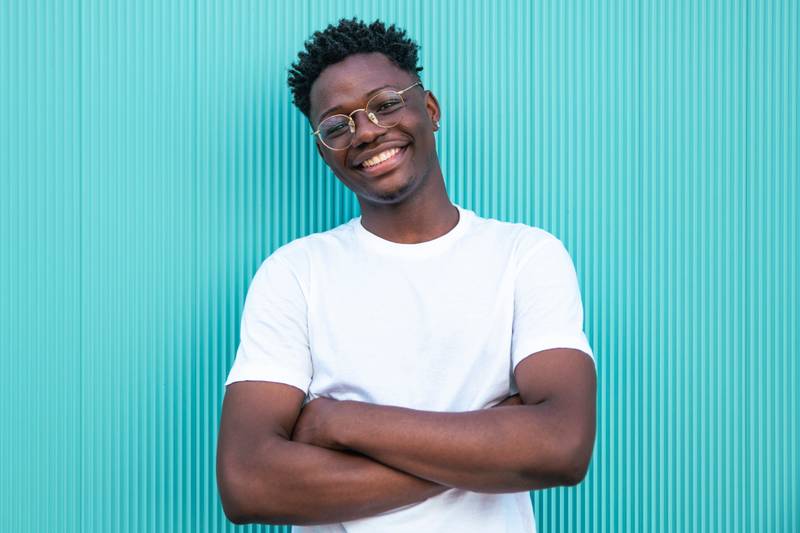 Happy young african american man smiling with arms crossed on turquoise background - Portrait of a cheerful young man - Happines and positive concept