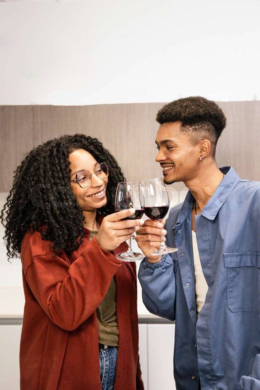 Happy young man and woman drinking with glasses in home. Cheering diverse couple toasting with wine in kitchen.