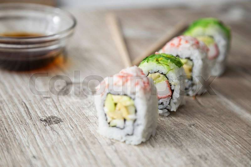 wooden texture with arranged sushi rolls next to bowl with soy sauce and chopsticks