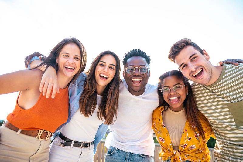 Low angle view of a happy group of multiracial friends looking at camera, enjoying outdoors. Multiethnic cheerful young people