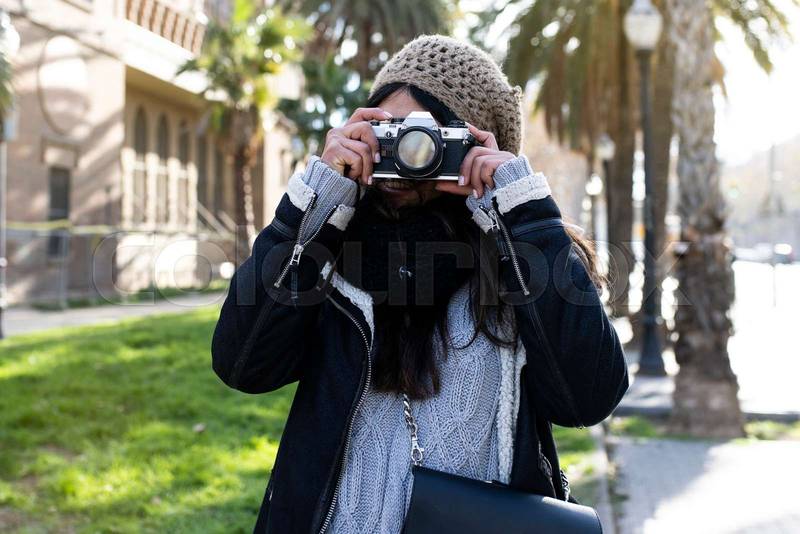 smiling woman traveler holding a camera at the city in holidays - relaxation, tourism concept